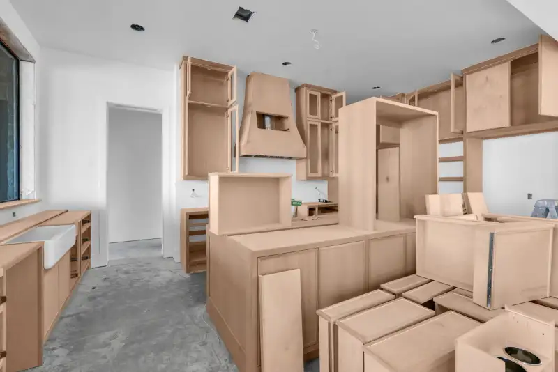 Unfinished kitchen with light wood cabinets, a range hood, a central island, and a farmhouse sink at left.