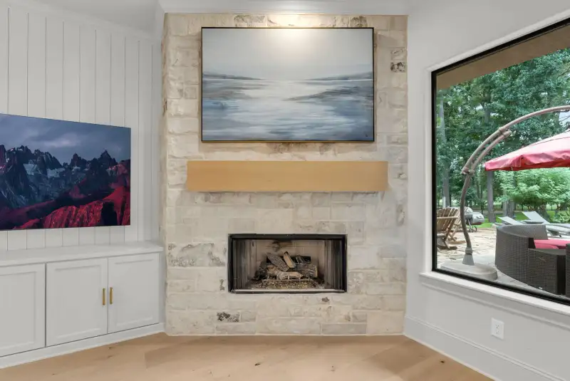 Stone fireplace with a wood mantel, built-in cabinets, and a window overlooking a covered patio.