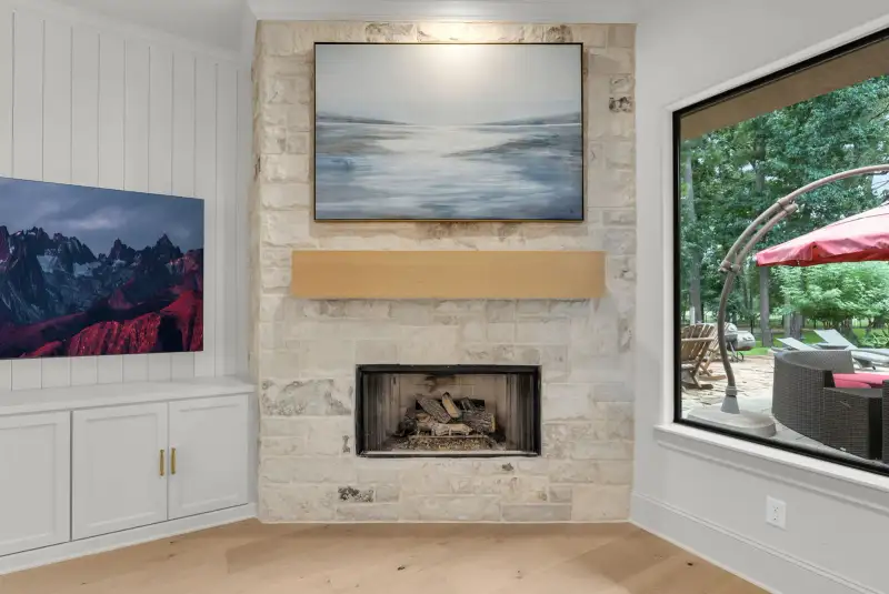 Stone fireplace with a wood mantel, built-in cabinets, and a window overlooking a covered patio.