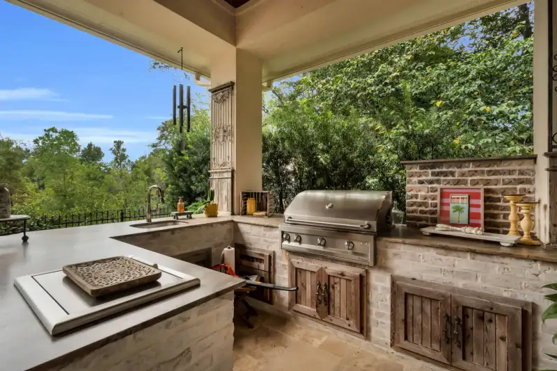 Outdoor kitchen with a stainless steel grill, stone counters, a sink, and brick cabinetry under a covered patio.