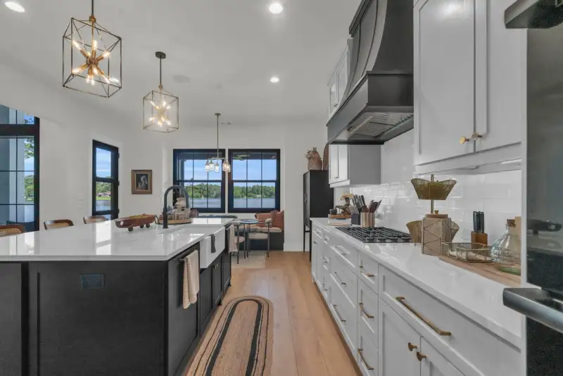 Kitchen with a dark island, white cabinets, a black range hood, and a view through windows to the dining nook.