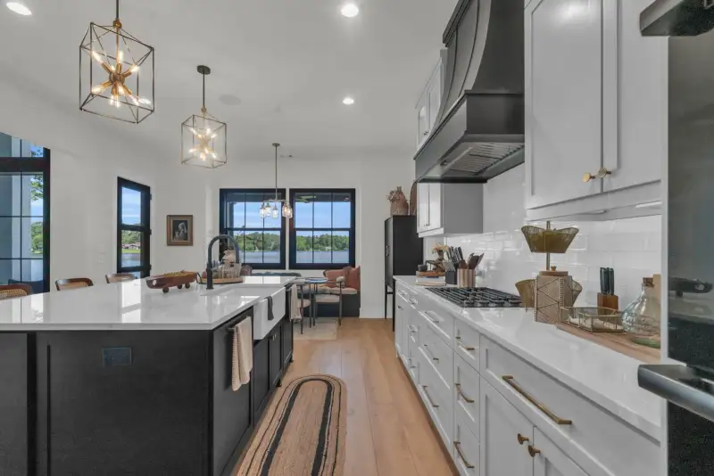 Kitchen with a dark island, white cabinets, a black range hood, and a view through windows to the dining nook.