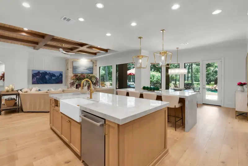Open kitchen with a farmhouse sink island, a waterfall island with bar stools, and glass doors to the backyard.