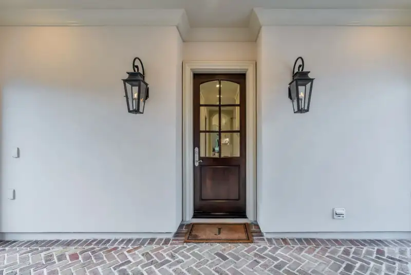 Front entry with a dark wood door, two wall lanterns, and a herringbone brick walk.