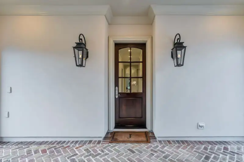 Front entry with a dark wood door, two wall lanterns, and a herringbone brick walk.