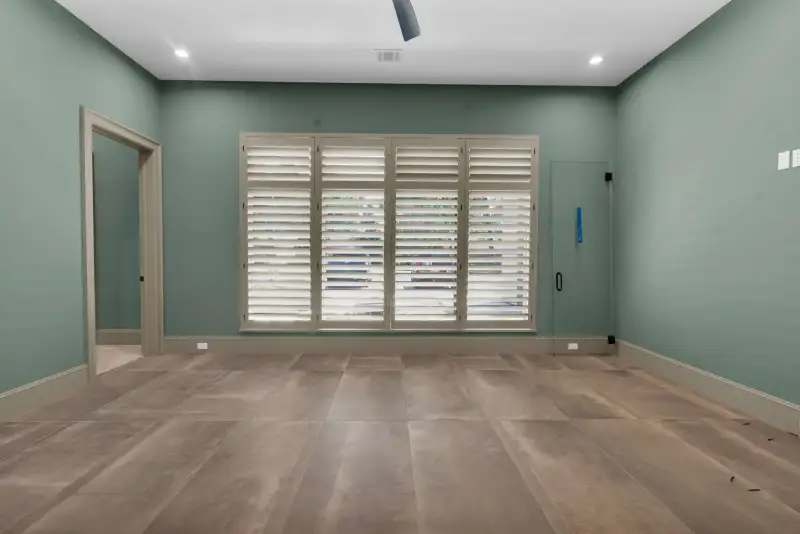 Room with green walls, plantation shutters over the window, and a tile floor.