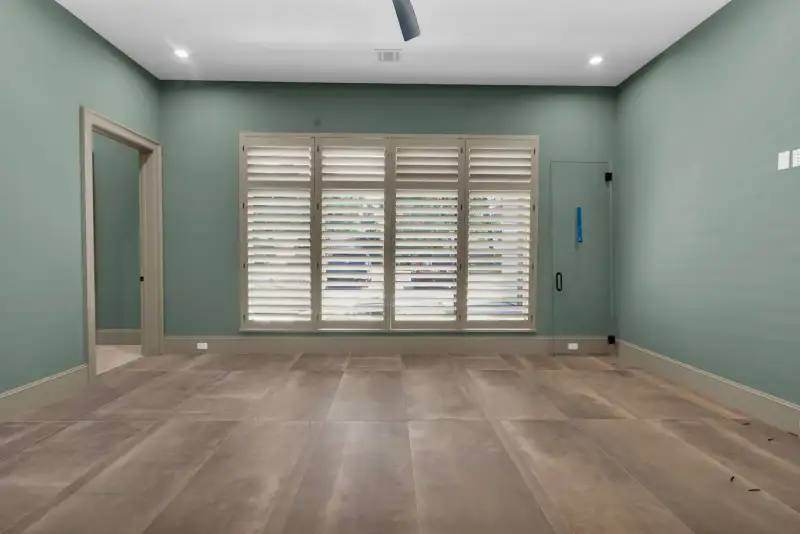 Room with green walls, plantation shutters over the window, and a tile floor.