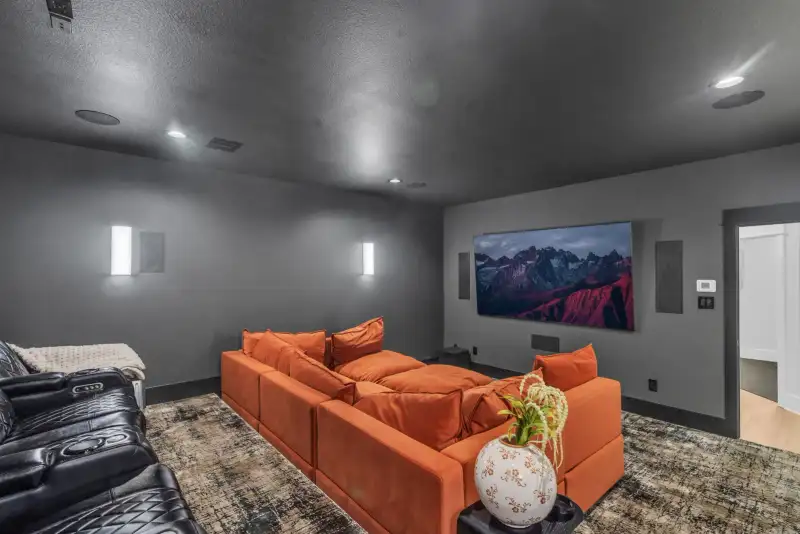Media room with an orange sectional, a wall-mounted screen, and recessed lighting.