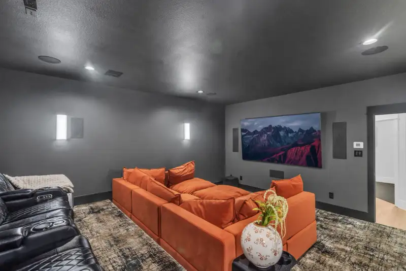 Media room with an orange sectional, a wall-mounted screen, and recessed lighting.