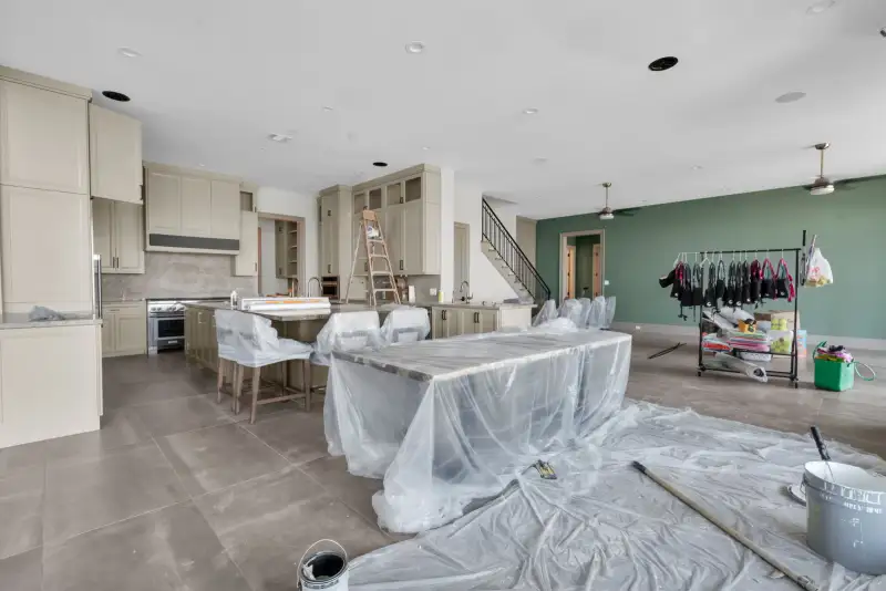 Open kitchen and family area with a green accent wall, ceiling fans, and a staircase near the center.