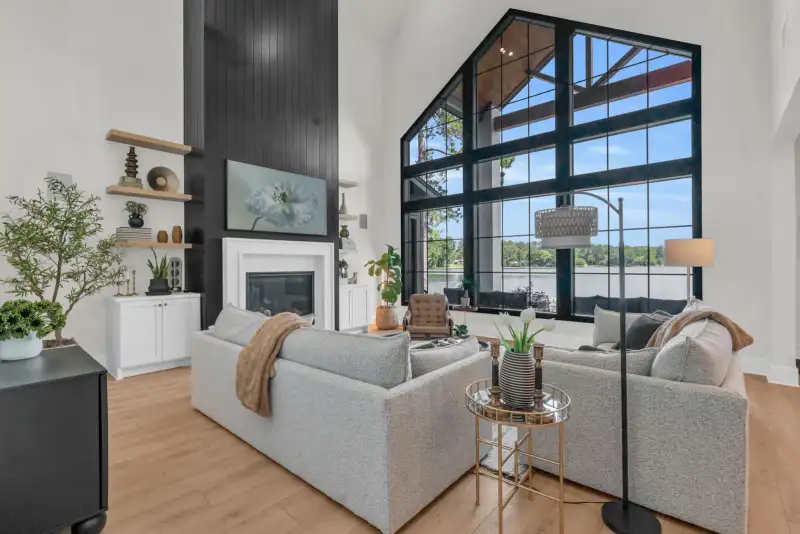 Living room with a black shiplap fireplace wall, a tall black-framed window, and gray sofas on light oak flooring.