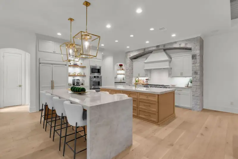Kitchen with a waterfall island with bar stools, a light wood island, and two gold pendant lights.