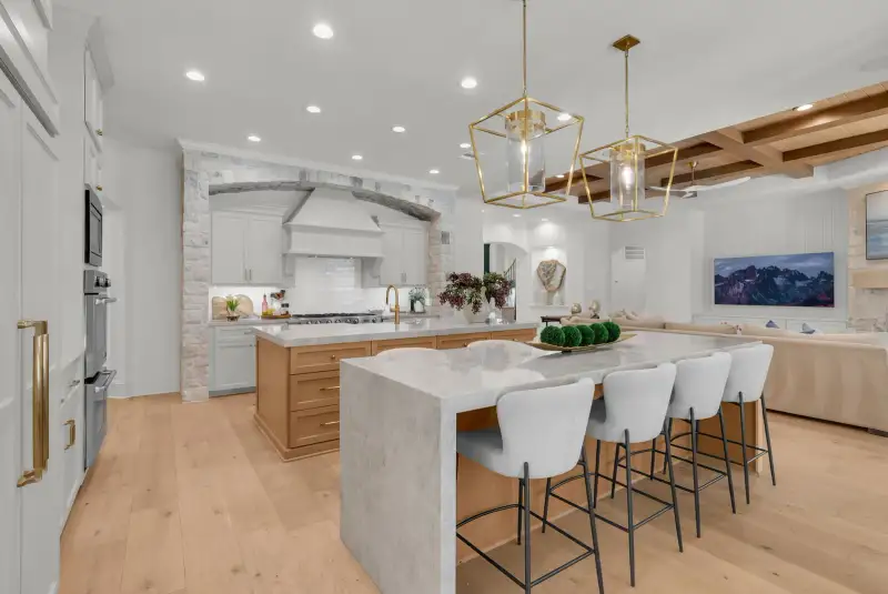 Kitchen with a stone arch over a range hood, a waterfall island with bar stools, and a living area beyond.