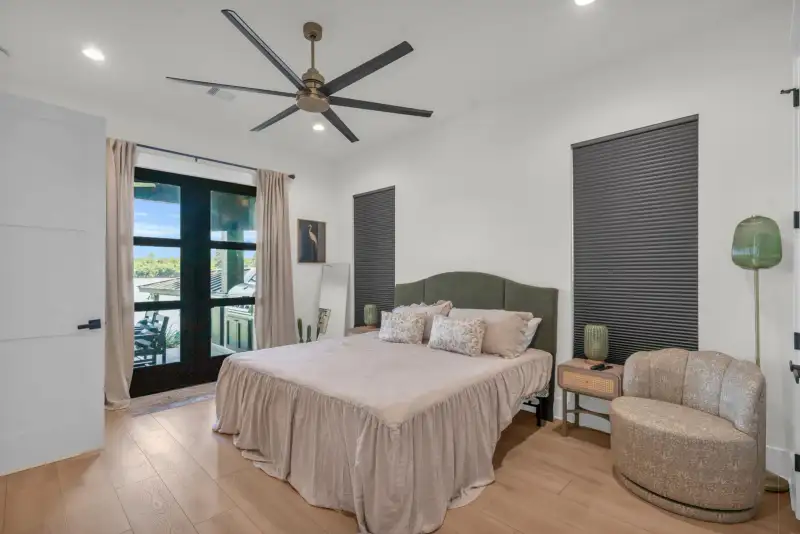 Bedroom with a green upholstered headboard, dark roller shades, a ceiling fan, and glass doors.