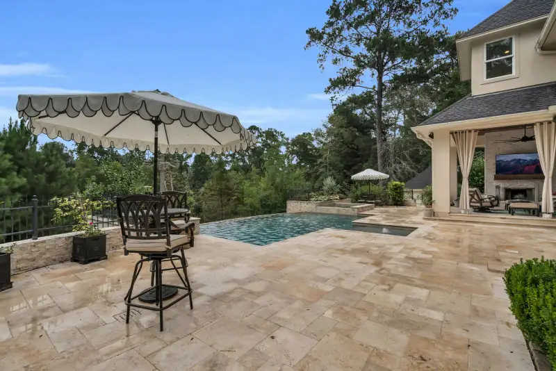 Pool deck with stone pavers, a scalloped umbrella, a bar table, and the rear of the house.