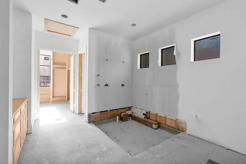 Unfinished room with a light wood base cabinet at left and three small windows on a white wall.