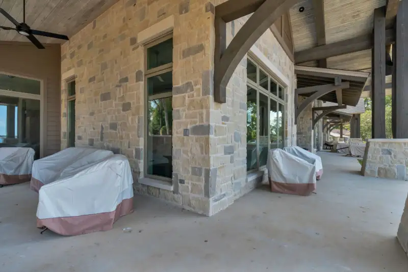 Covered patio with stone walls, wood beams, and furniture under covers.