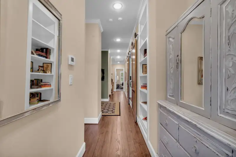 Hallway with built-in white bookshelves, a distressed white cabinet, wood floors, and a runner rug.