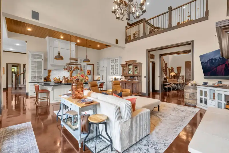 Open living room with a wood-paneled ceiling, a white kitchen island with pendant lights, and a cream sofa.