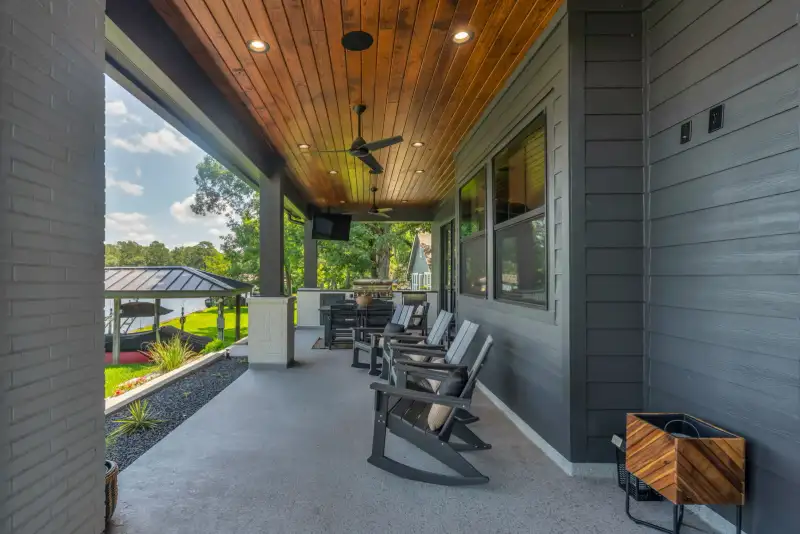 Covered porch with a wood ceiling, rocking chairs, and a side table beside gray siding.