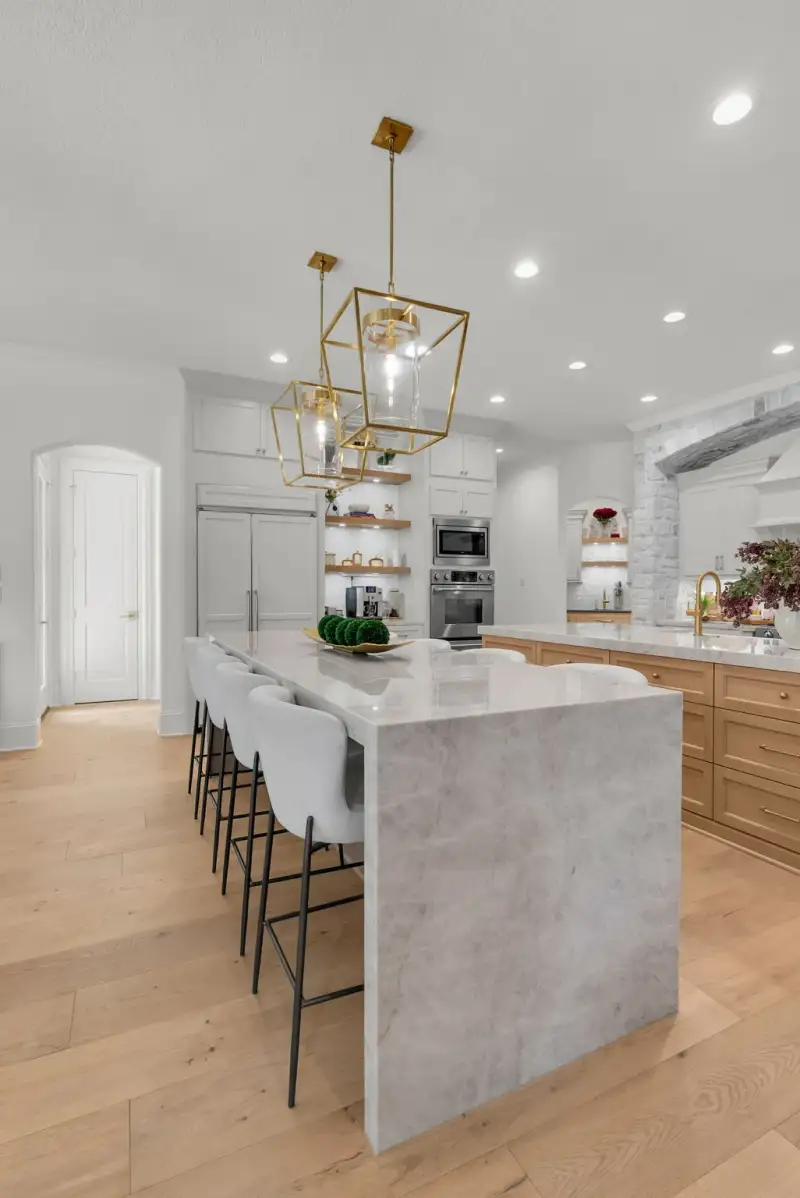Kitchen island with a waterfall marble-look countertop, gray bar stools, and gold pendant lights.