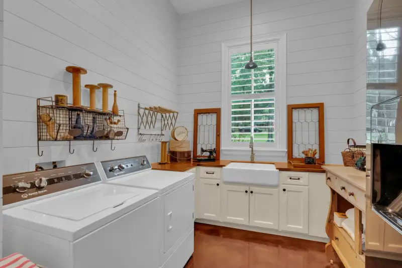 Laundry room with white shiplap walls, a white washer and dryer, a farmhouse sink, and white cabinets.