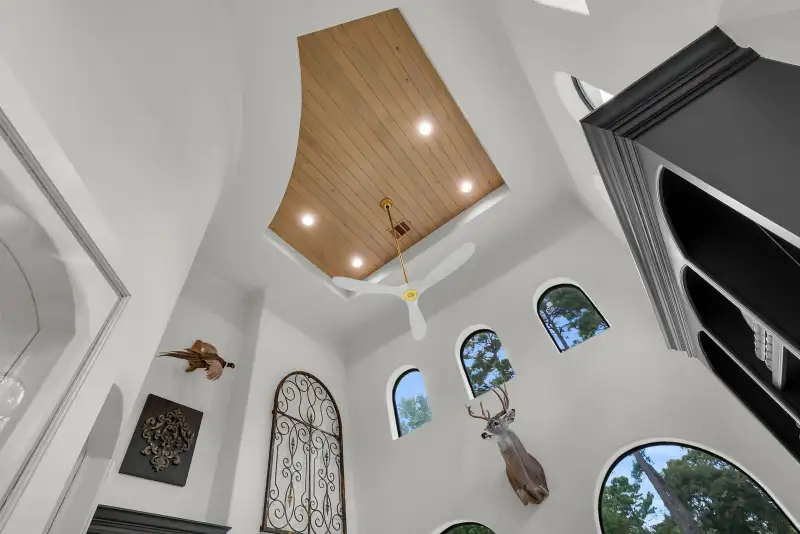 Upward view of a wood plank ceiling with recessed lights, a ceiling fan, and arched windows.