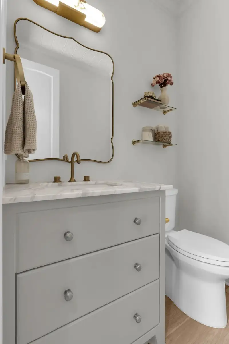 Powder room with a gray vanity, a marble-look top, a brass-edged mirror, and a toilet.