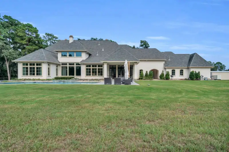 Rear elevation of a stucco home with a wide lawn, a covered patio, and a row of windows.