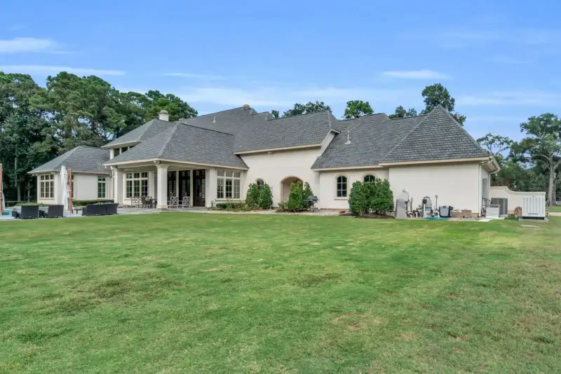 Rear elevation of a stucco home with a covered patio, arched side gallery, and a broad lawn.