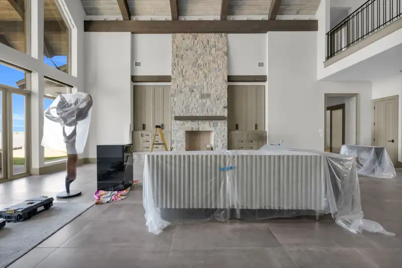 Room with a stone fireplace, built-in cabinets on each side, and covered furniture on the floor.