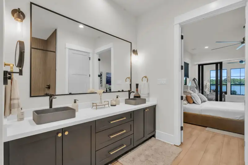 Bathroom double vanity with gray vessel sinks and a doorway into a bedroom with glass sliding doors.