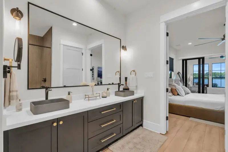 Bathroom double vanity with gray vessel sinks and a doorway into a bedroom with glass sliding doors.