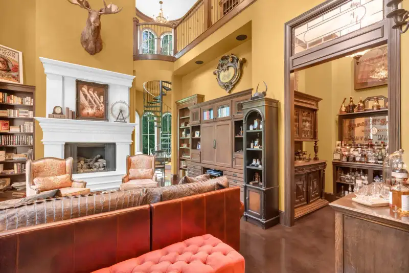 Living room with a white fireplace mantel, leather sofa, bookcases, and a view through to a spiral staircase.