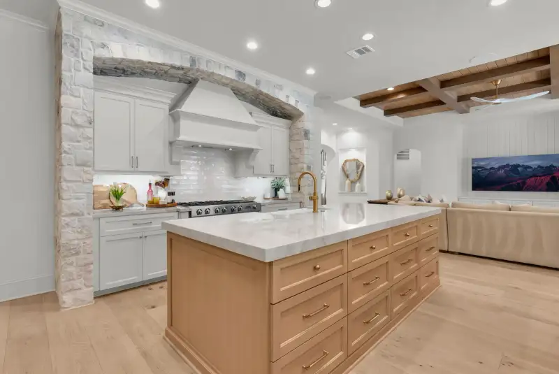 Kitchen island with a light wood base in front of a stone arch over a range hood.