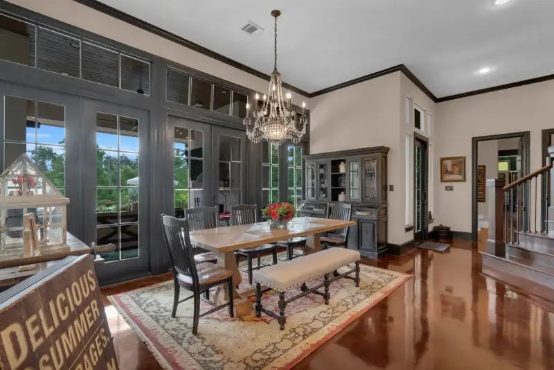 Dining room with a wood table, an upholstered bench, a crystal chandelier, and black-framed French doors.