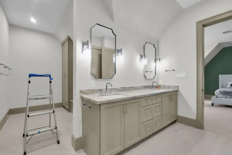Bathroom with a double vanity, a step ladder, and a doorway to a bedroom beyond.