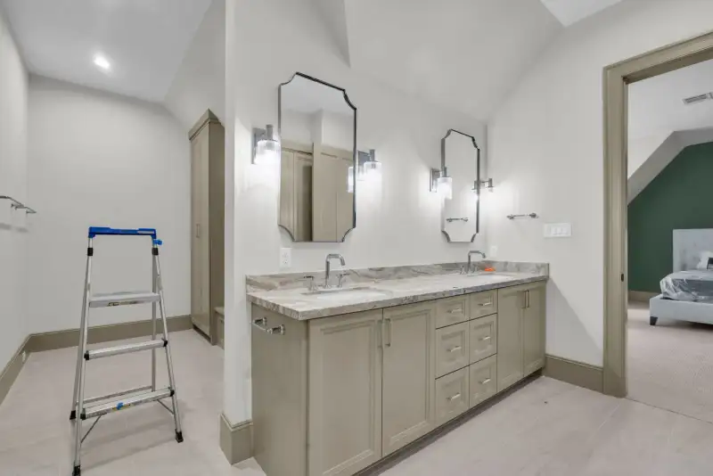 Bathroom with a double vanity, a step ladder, and a doorway to a bedroom beyond.