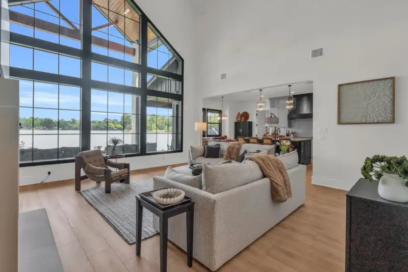Open living room with two-story black-framed windows, a light sofa, and a view into the kitchen.