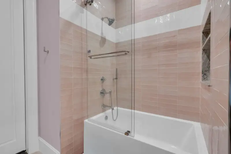 Bathtub and shower with pink wall tile, a glass enclosure, and chrome fixtures.