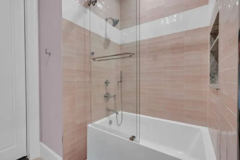 Bathtub and shower with pink wall tile, a glass enclosure, and chrome fixtures.