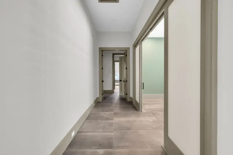 Hallway with gray tile floor, white walls, and doorways at the far end.