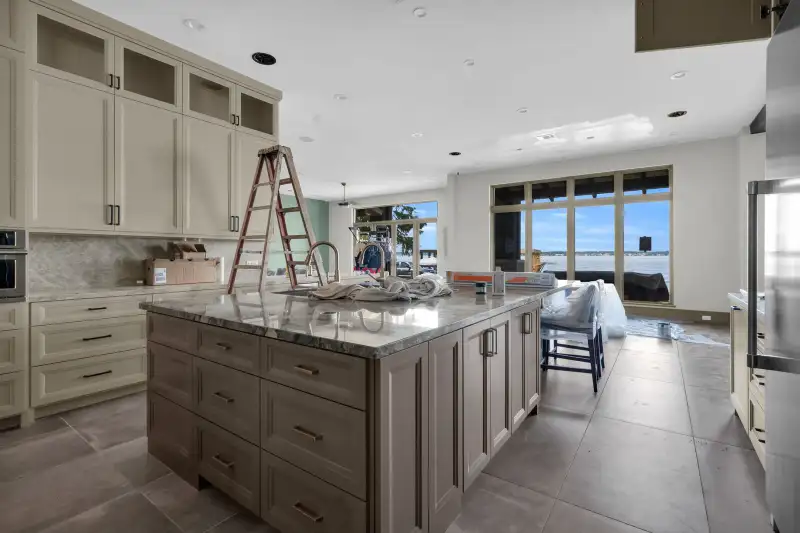 Kitchen island with a veined stone countertop, with windows and water visible in the background.