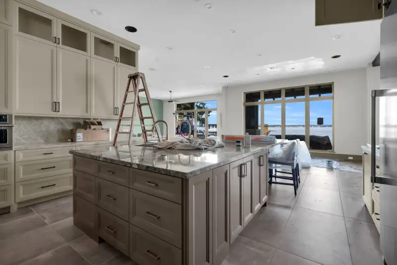 Kitchen island with a veined stone countertop, with windows and water visible in the background.