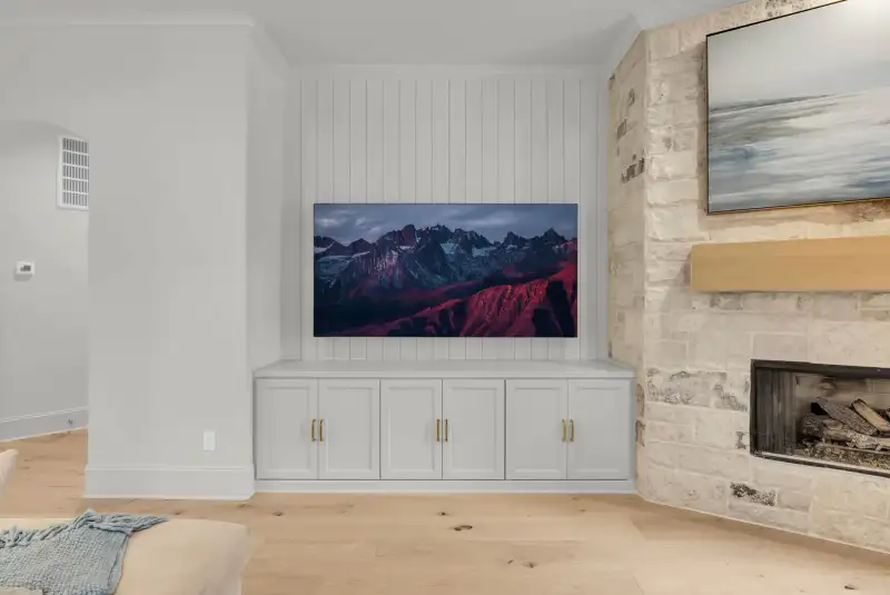 Media wall with a wall-mounted television over built-in white cabinets, beside a stone fireplace.