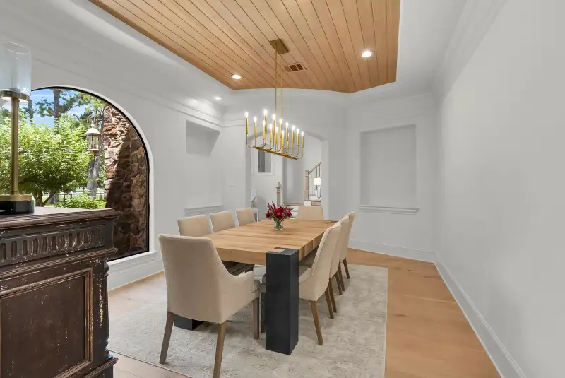 Dining room with a wood plank tray ceiling, a gold chandelier, and an arched window with a view outdoors.