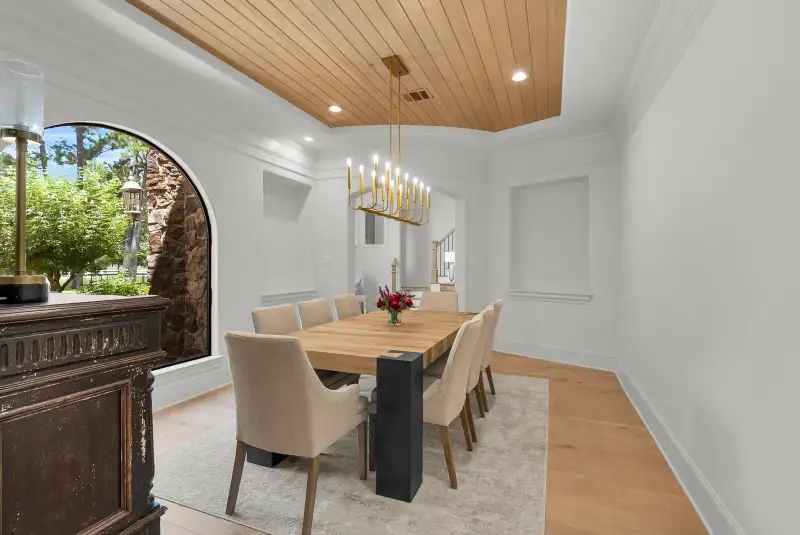 Dining room with a wood plank tray ceiling, a gold chandelier, and an arched window with a view outdoors.