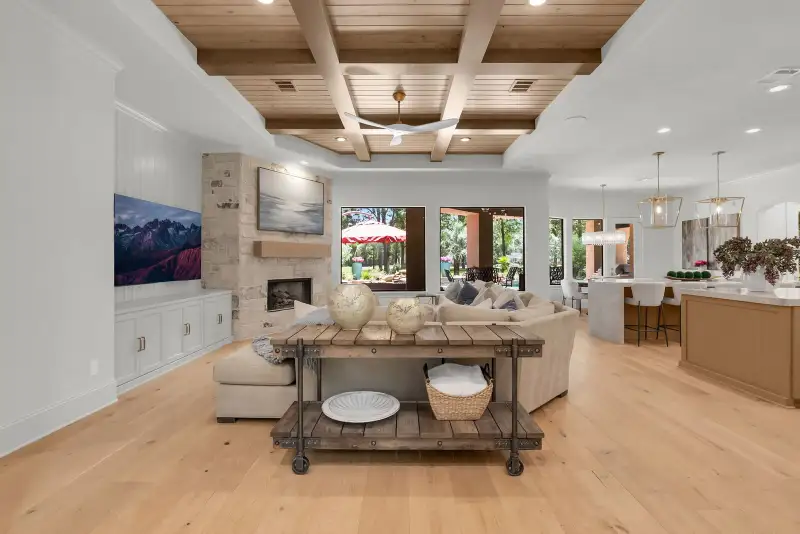 Living room with a coffered wood ceiling, a stone fireplace, a wall-mounted television, and a sectional sofa.