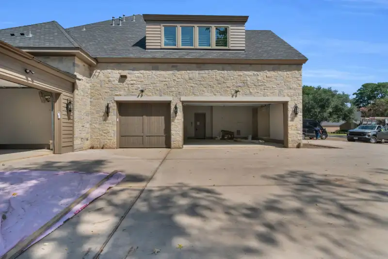 Rear exterior of the Escondido home with stone walls, two garage bays, and a concrete drive.
