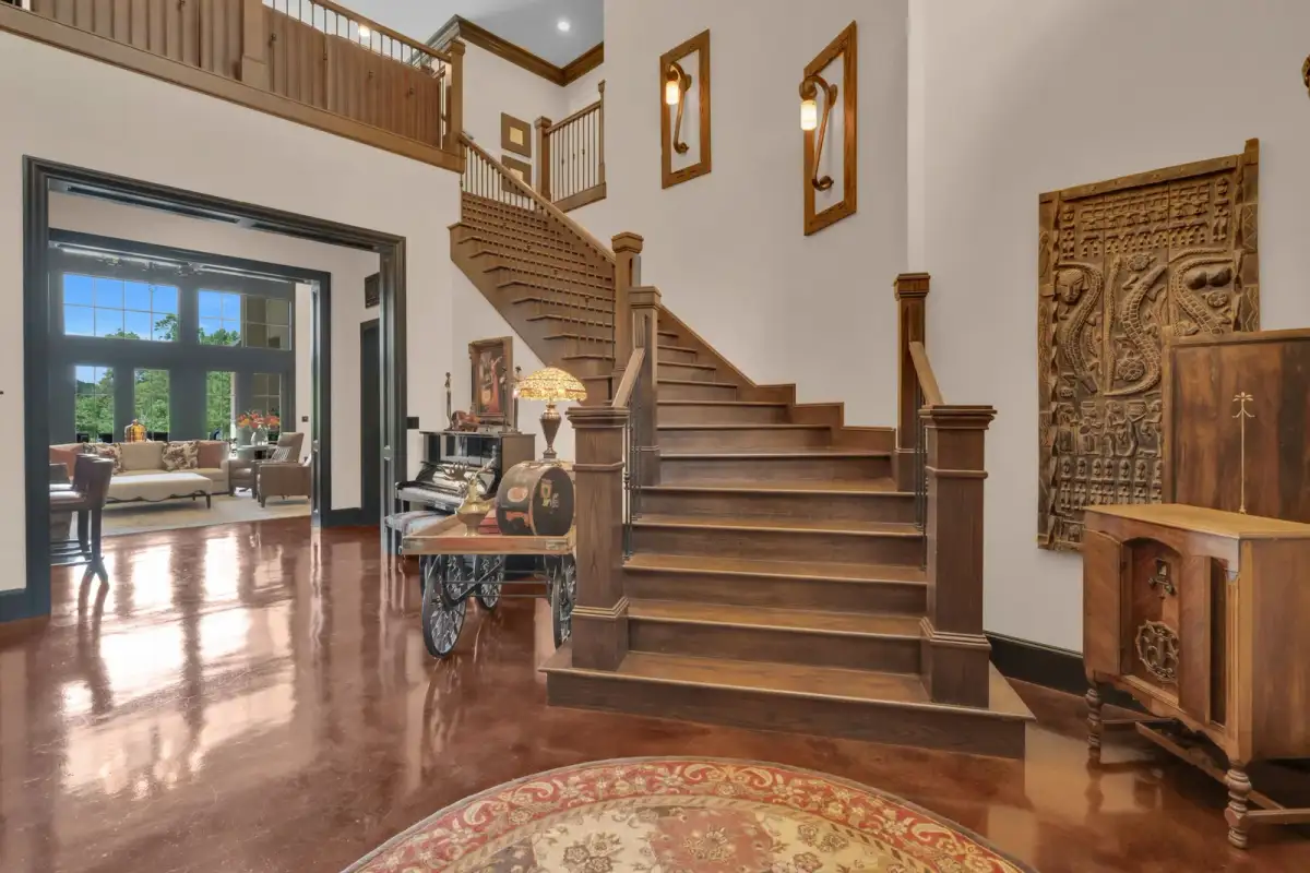Entry foyer with a curved wood staircase, stained concrete floors, a cart display, and a carved wood wall panel.